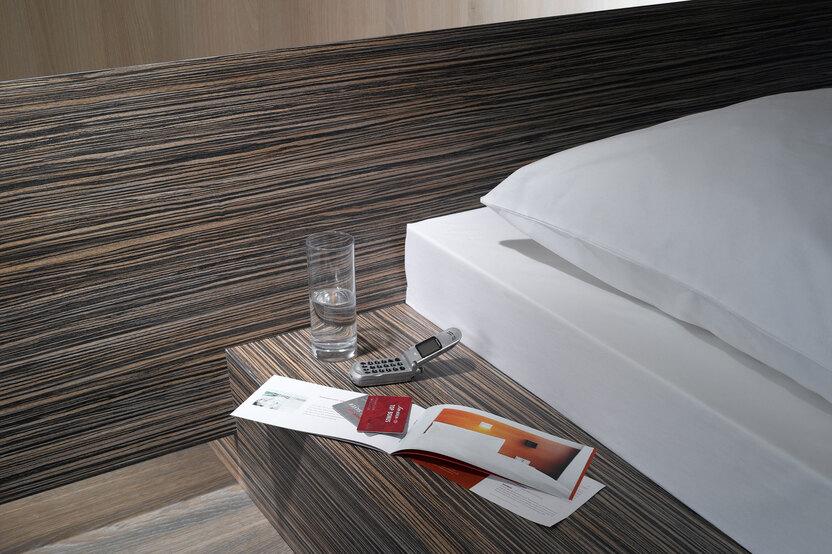 Detailaufnahme von Bettumrandung in dunklem Holz mit Ablagemöglichkeit