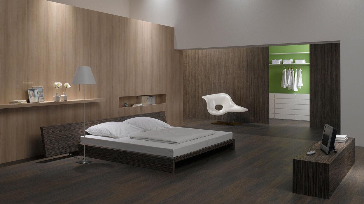 Schlafzimmerimpression von Bett, Nachtisch und Sideboard mit Holzverkleidung an Wand und indirektert Beleuchtung