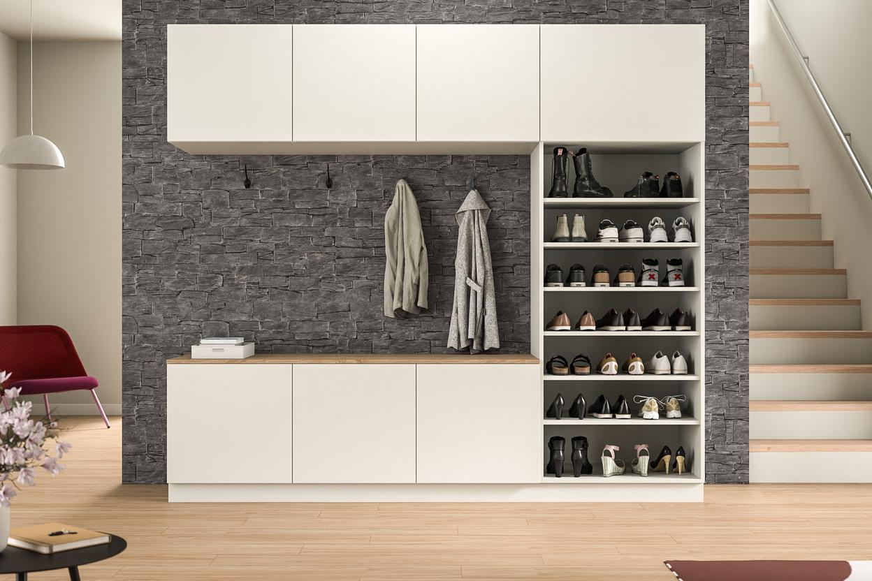 Maßgefertigter Schrankwand mit integrierter Garderobe im Eingangsbereich. Eine stilvolle Schrankwand nach Maß in weißer Farbe mit Schubfächern und einer offenen Nische für Jacken, vor einer markanten Steinwand, im Eingangsbereich.