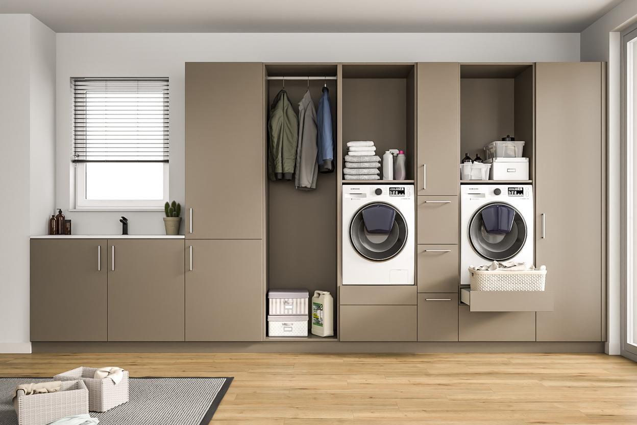 Modern gestalteter Wirtschaftsraum mit maßgefertigten Schränken. Ein heller Raum mit einem großen, maßgeschneiderten Schranksystem in Taupe, integrierten Waschmaschinen, Ablageflächen und einem Fenster mit Jalousien.